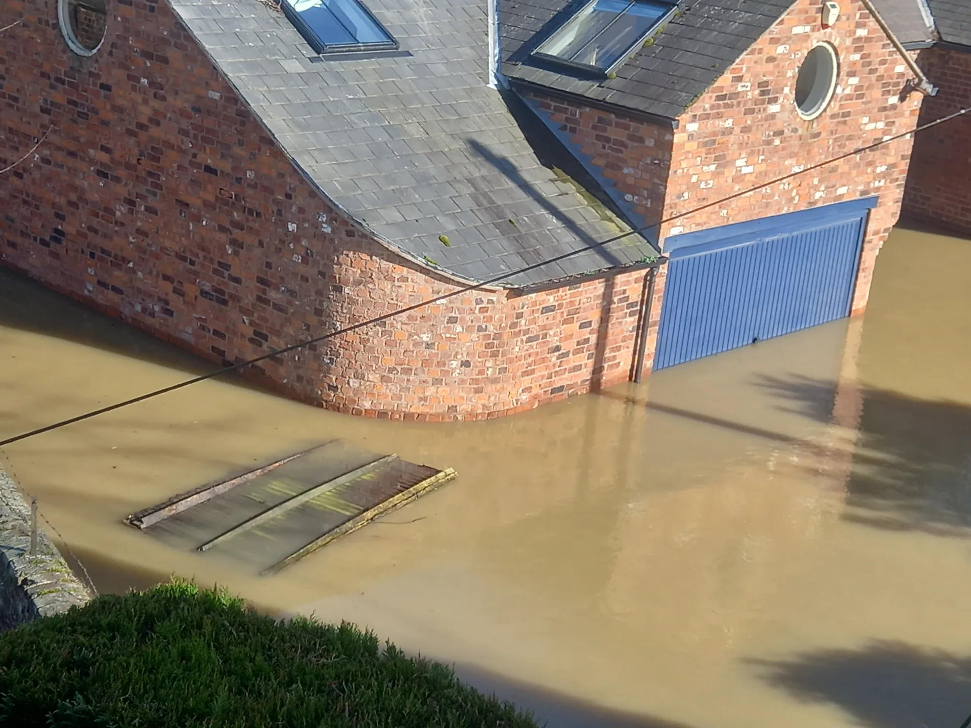 Floodwater surrounding a brick outbuilding and covering its garage doors